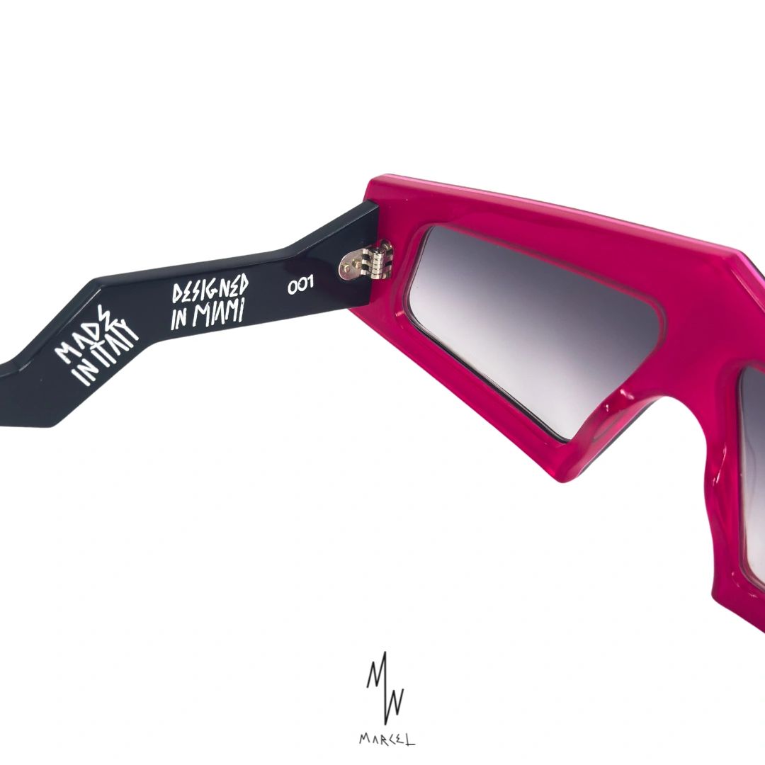 Pink sunglasses with black arm labeled 'Designed in Miami' on a white background. Close up view of internal engraving.