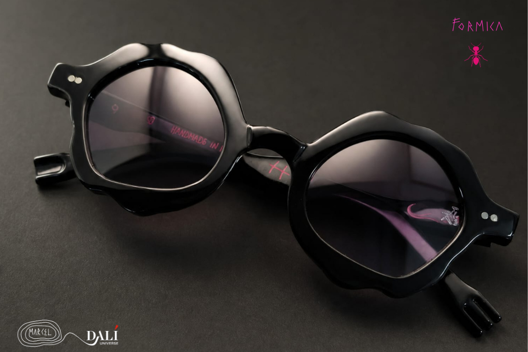 Black round sunglasses with thick sculptural frames and dark tinted lenses, shown on a dark gray background. The image includes the text 'FORMICA' in pink and 'DALI' branding in the corners.