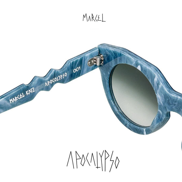 Blue sunglasses with 'Marcel' branding on a white background. Close-up of temple engraving.