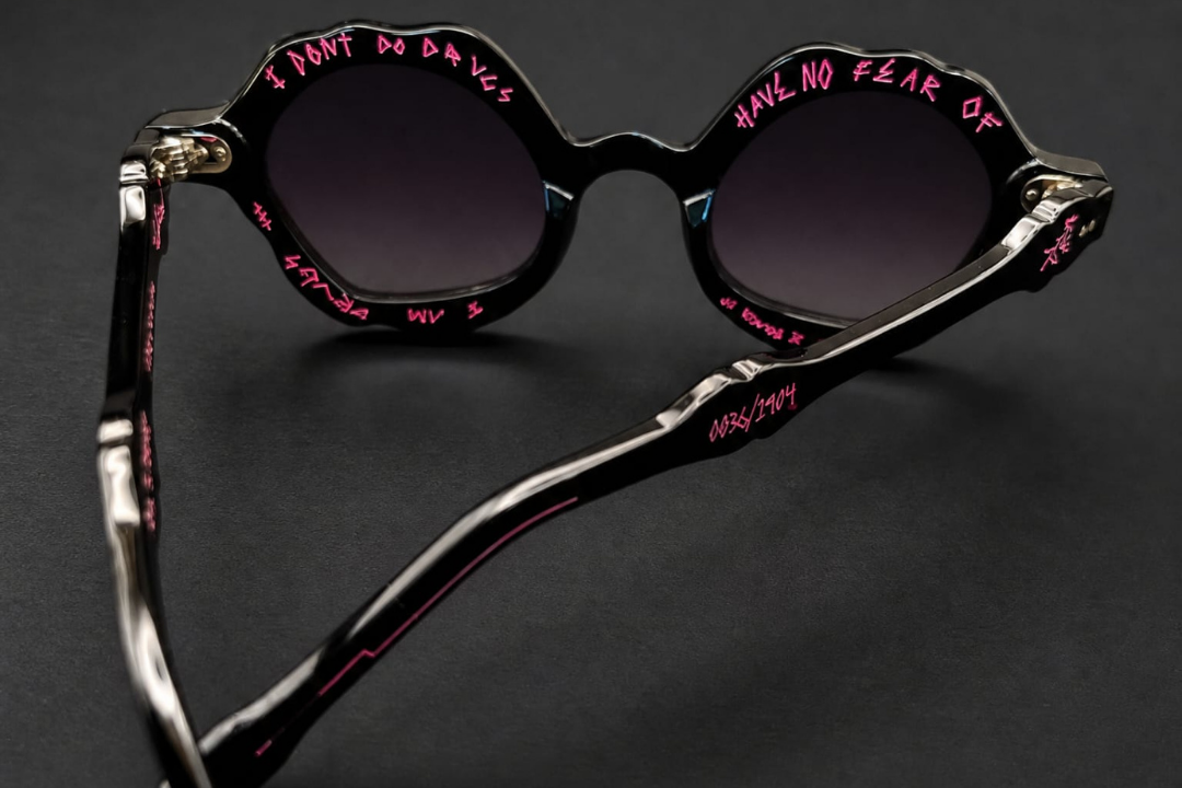A pair of round sunglasses with scalloped black frames, dark lenses, and pink handwritten text reading 'I DON'T DO DRUGS' and 'HAVE NO FEAR OF' on the rims, displayed on a dark background with Dali branding.