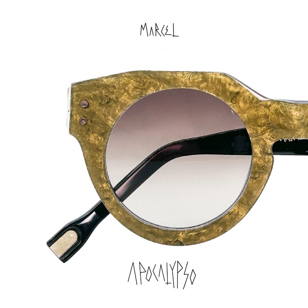 Gold-framed sunglasses with a white background, featuring the brand 'Marcel'. Close up of lenses.