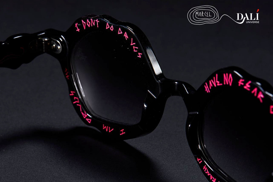 Black sunglasses with pink graffiti-style text on the lenses and frame, shown on a dark background with Dalli and Formica branding.