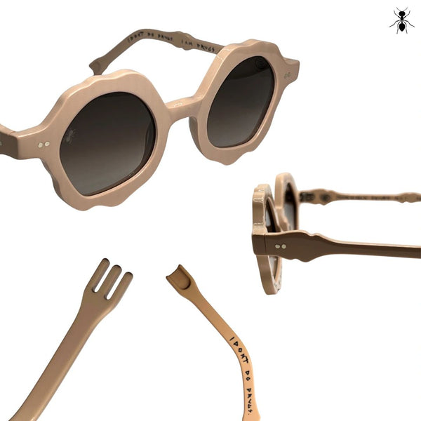 Beige sunglasses with unique frame design on a white background. Close up of temple pieces, lenses, and ear pieces.