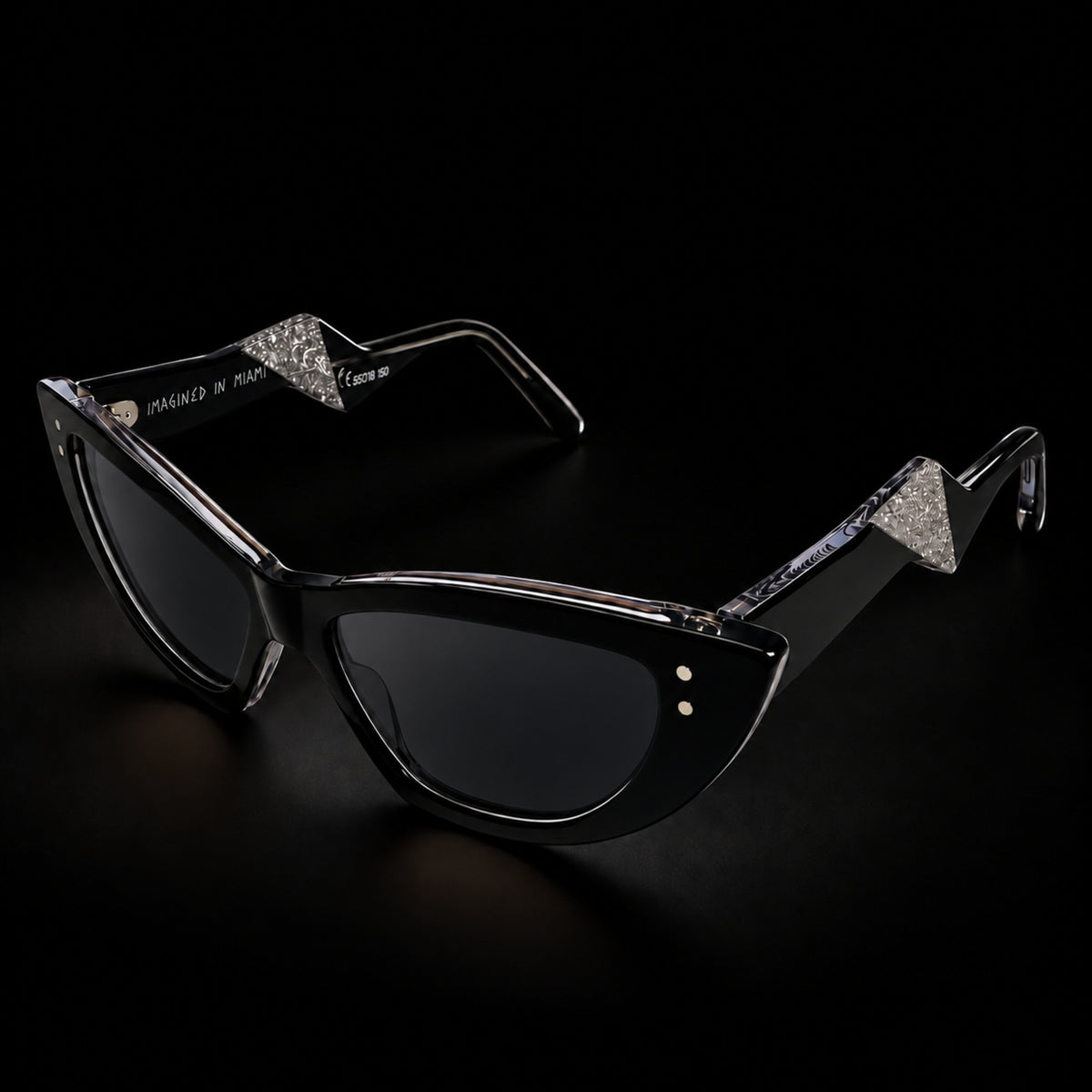 Black cat-eye sunglasses with black gradient lenses and clear temple tips, shown on a black background. The brand name 'MARCEL' is printed on the left lens. 3/4 view.