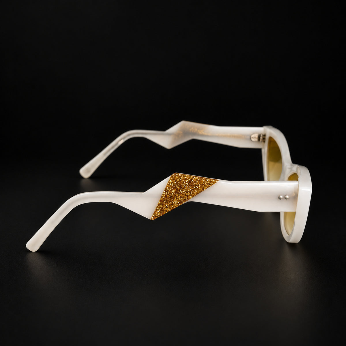 White and gold eyewear, black background, side profile view.