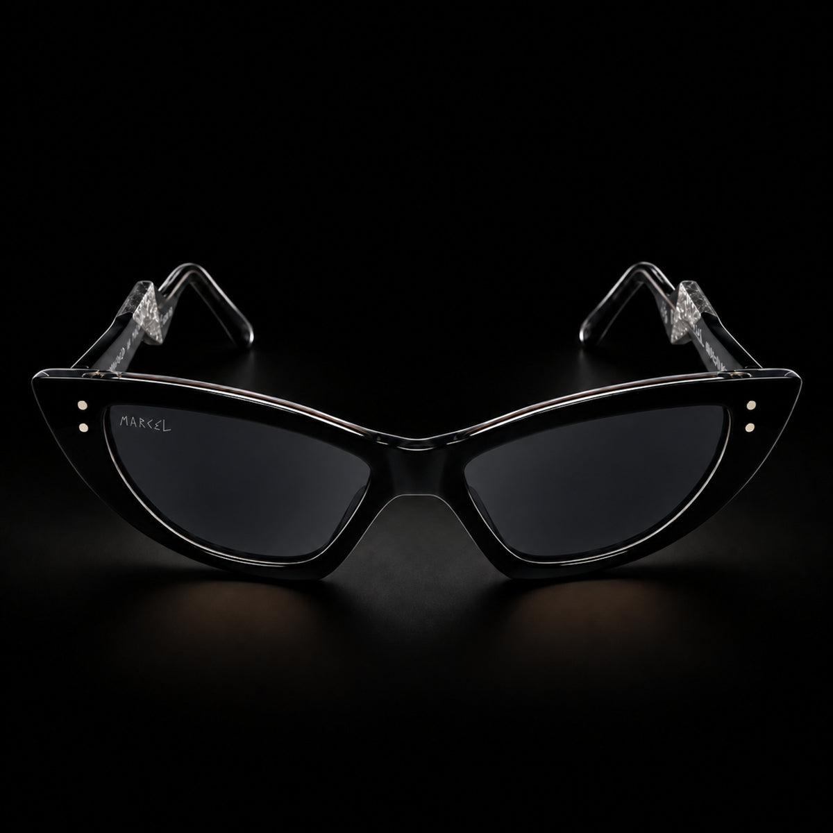 Black cat-eye sunglasses with black gradient lenses and clear temple tips, shown on a black background. The brand name 'MARCEL' is printed on the left lens. Front view.